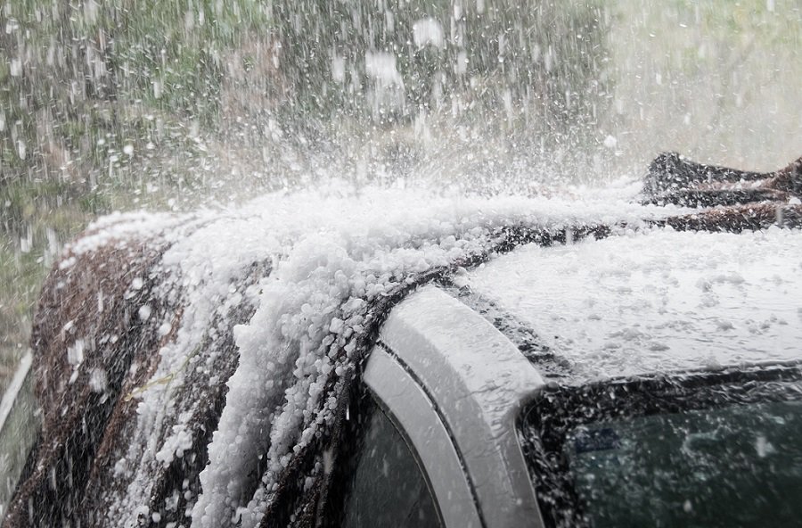 Heavy hail damaging a car roof during a hailstorm.