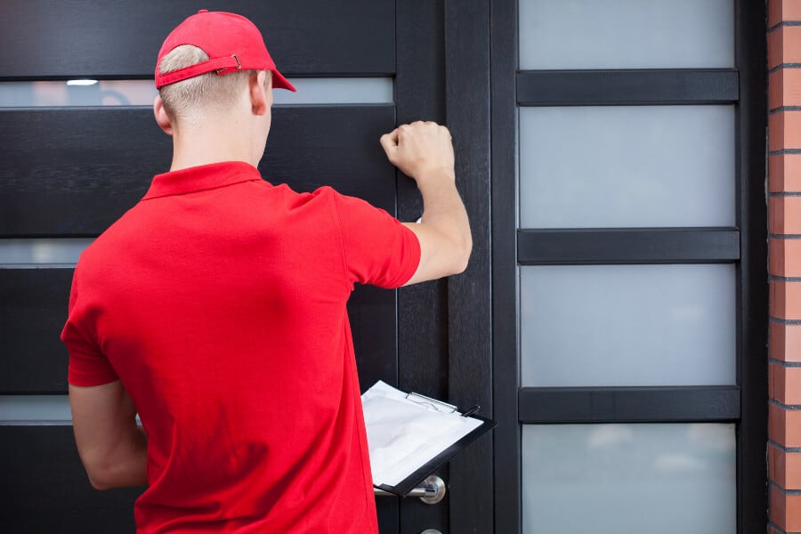 A hail damage repair service provider wearing a red shirt, knocking on a door.