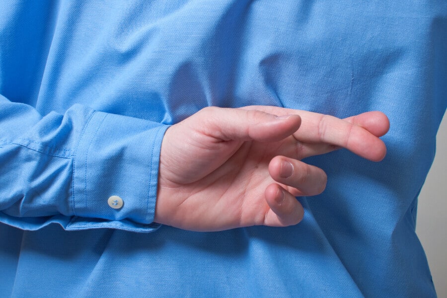 Close up of a man in a blue shirt crossing his fingers behind his back.