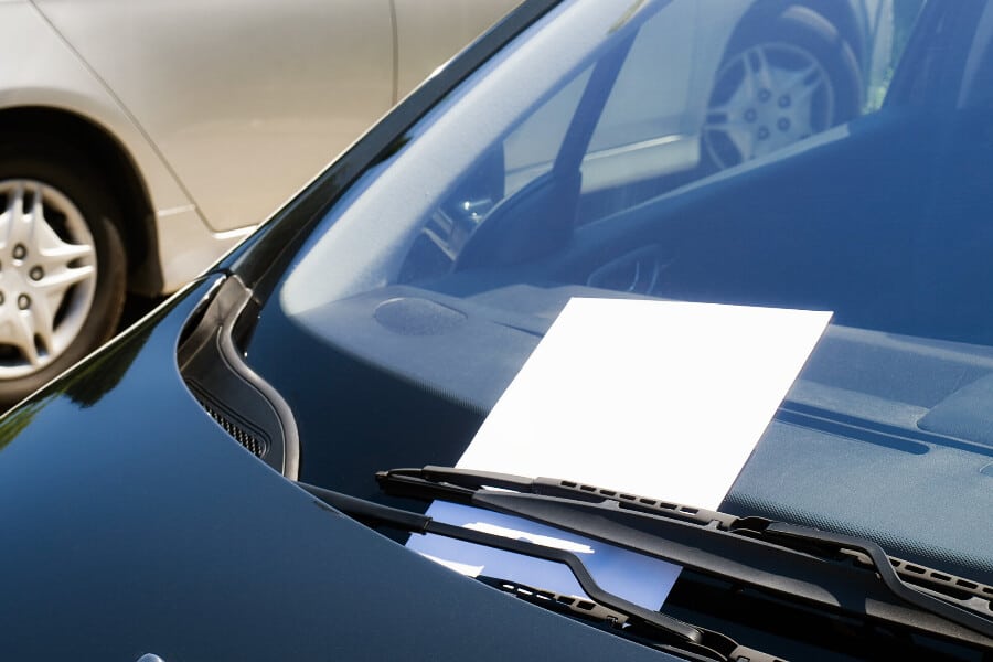 A piece of paper symbolizing a hail damage repair flyer left on a car windshield in a parking lot.