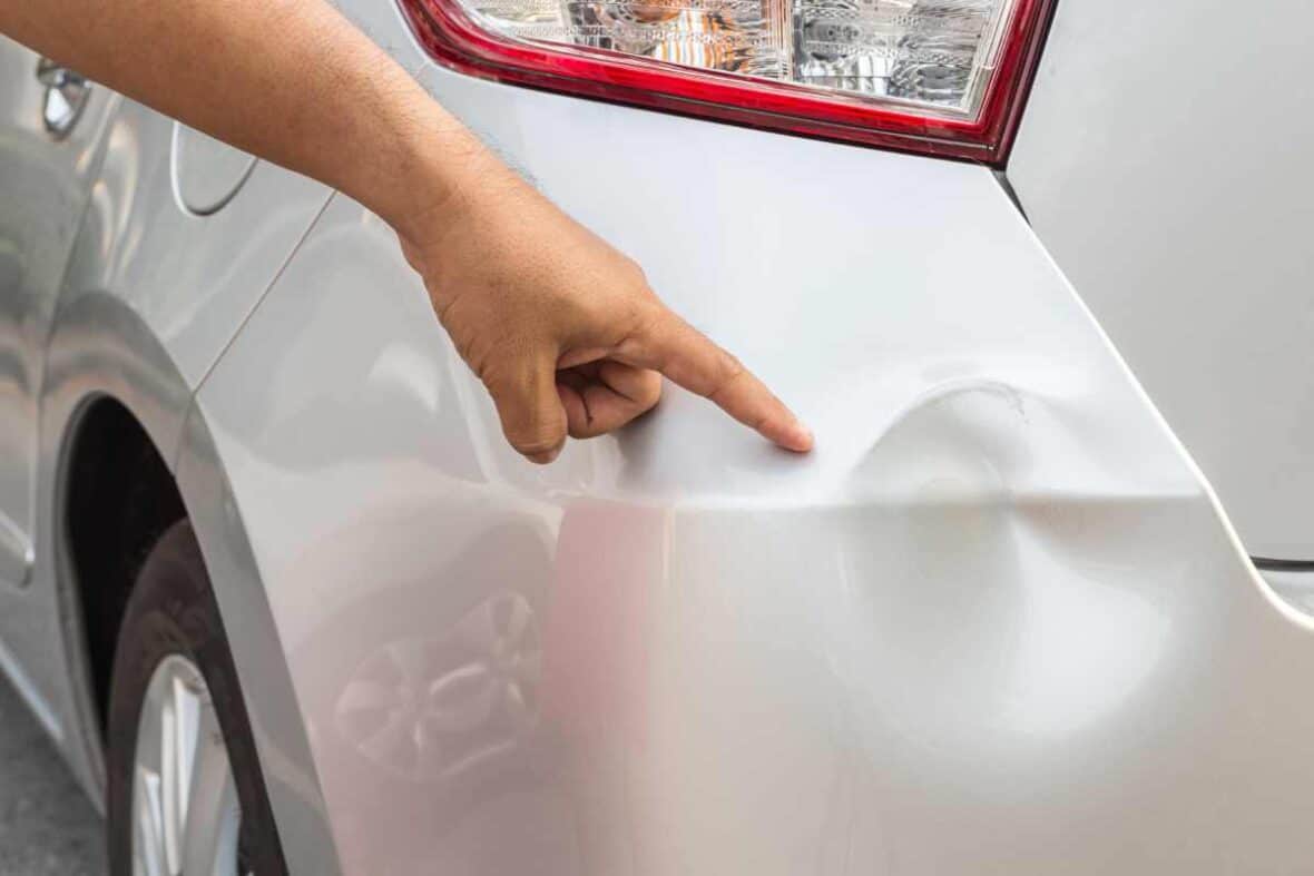 Expert PDR hail repair in Austin: Skilled hand pointing at a noticeable dent on the rear end of a sleek silver car