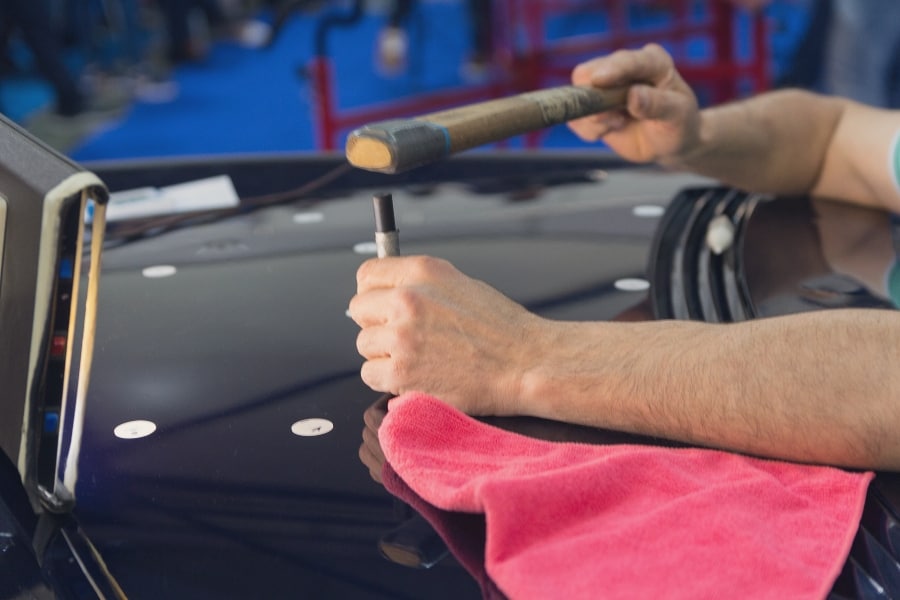 A technician in PDR in Lampasas removing hail dents from the hood of a car.