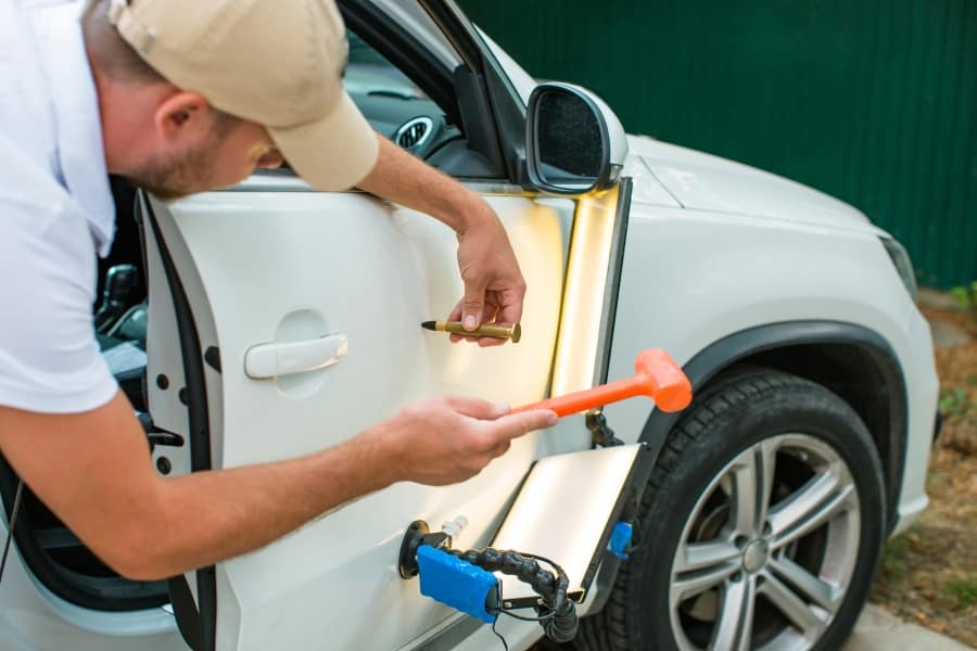 Man fixing car door by using methods of dent repair in Austin