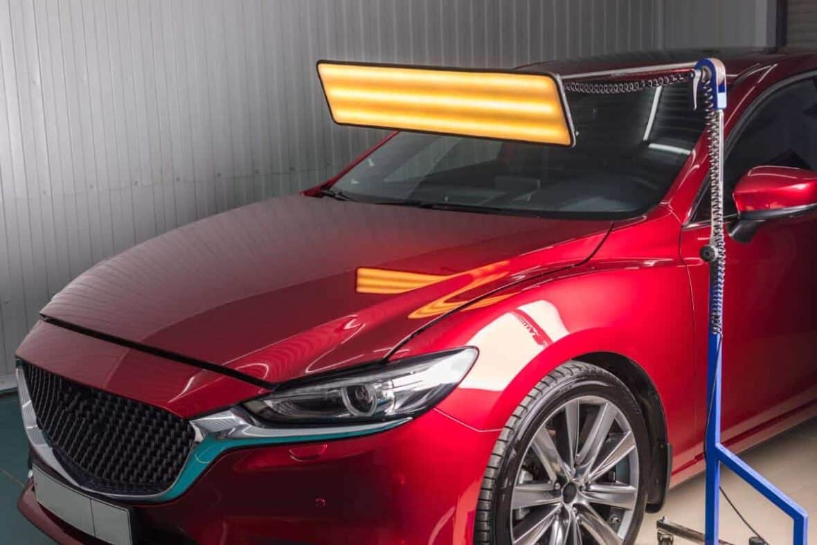 A red car being inspected with a light for a PDR estimate in Round Rock.