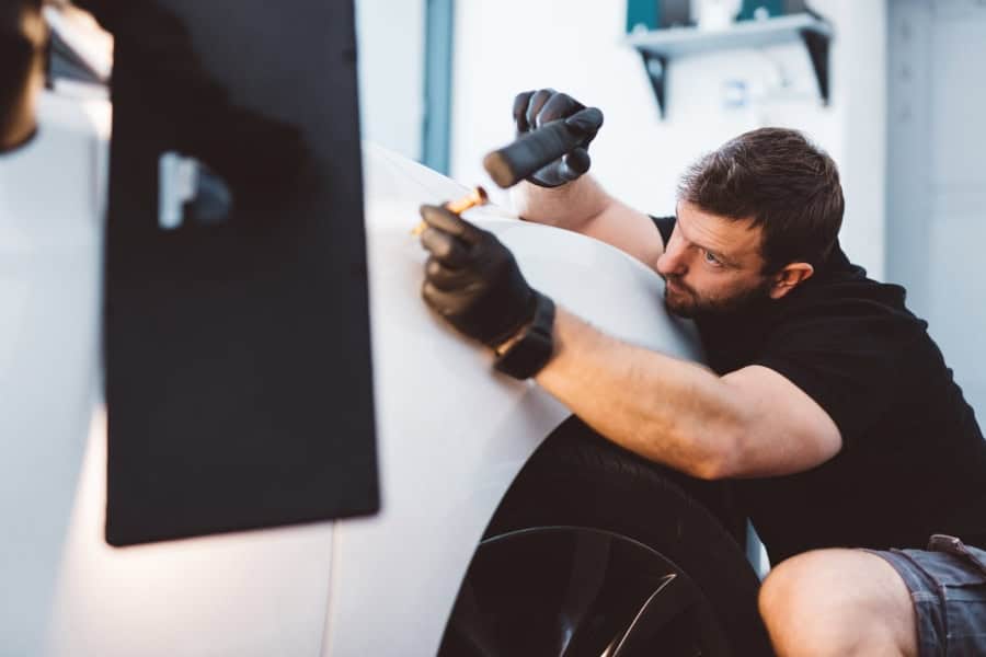 A technician at a Bastrop car ding repair shop works meticulously on a white vehicle.