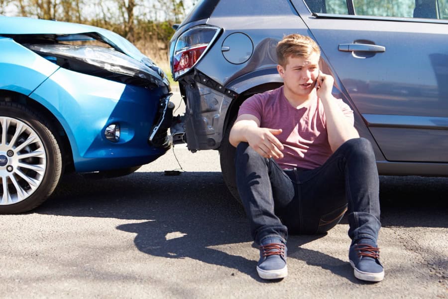 Man sitting by crashed cars, calling his insurance to discuss next steps and asking about Austin PDR.