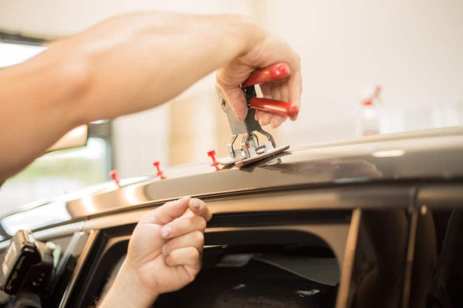 A technician using tools to perform Round Rock PDR on a car roof.