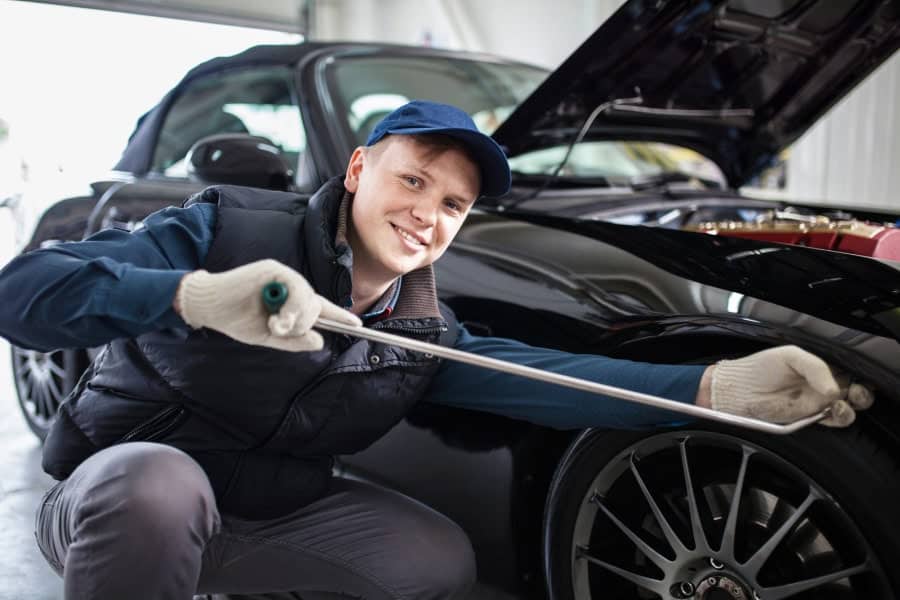 A mechanic smiling at Bastrop car dent repair shop, working on a black car.