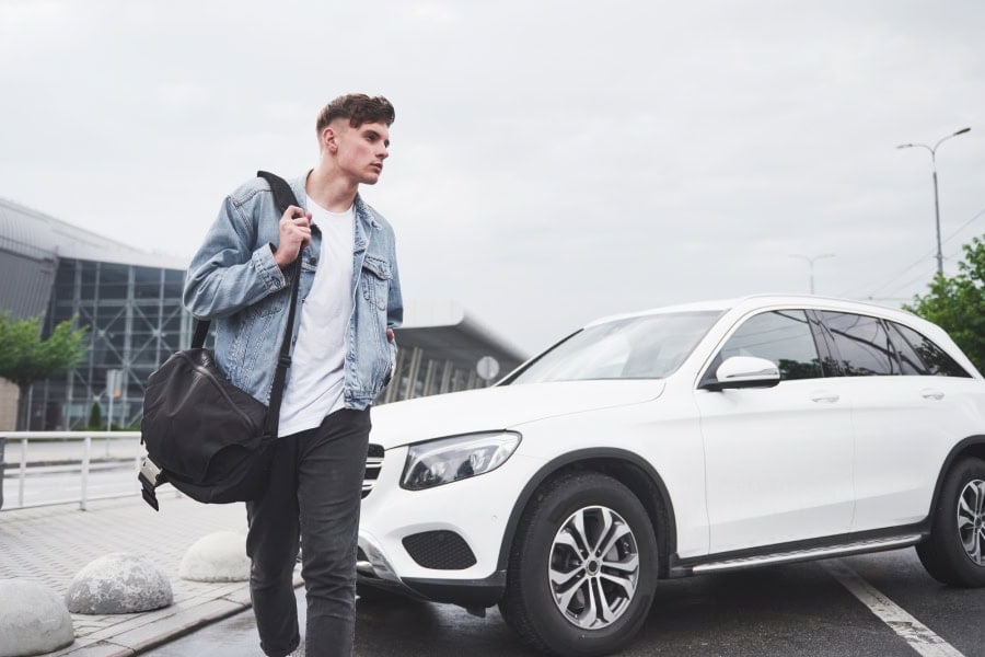 An image of a young collage student right next to his vehicle