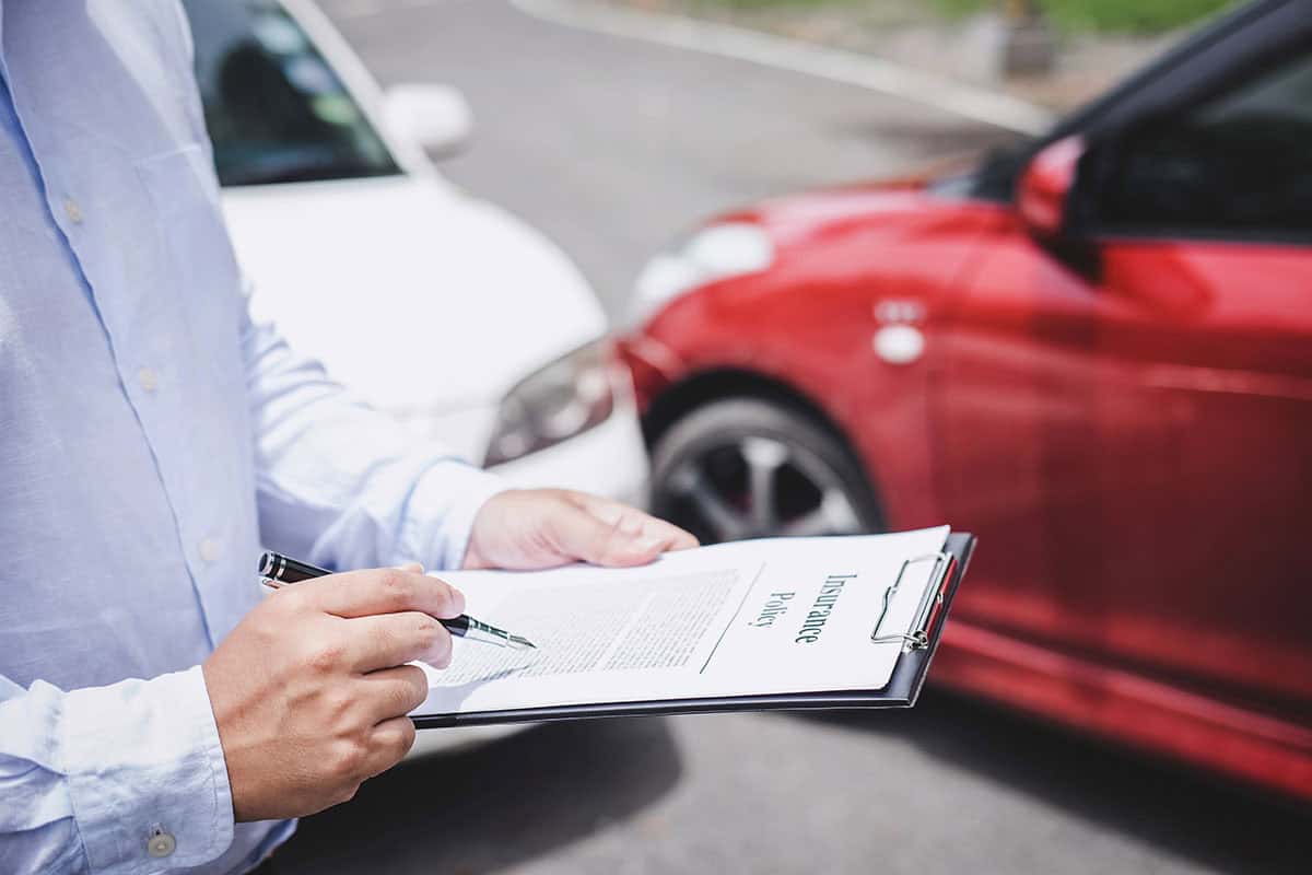 A man is filling out insurance paperwork on the scene of a fender bender accident.