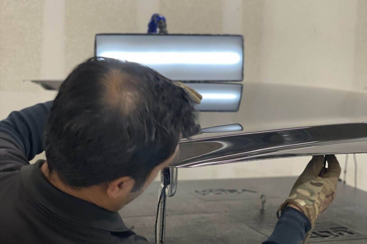 Paintless dent repair technician working on a vehicle body panel in the shop